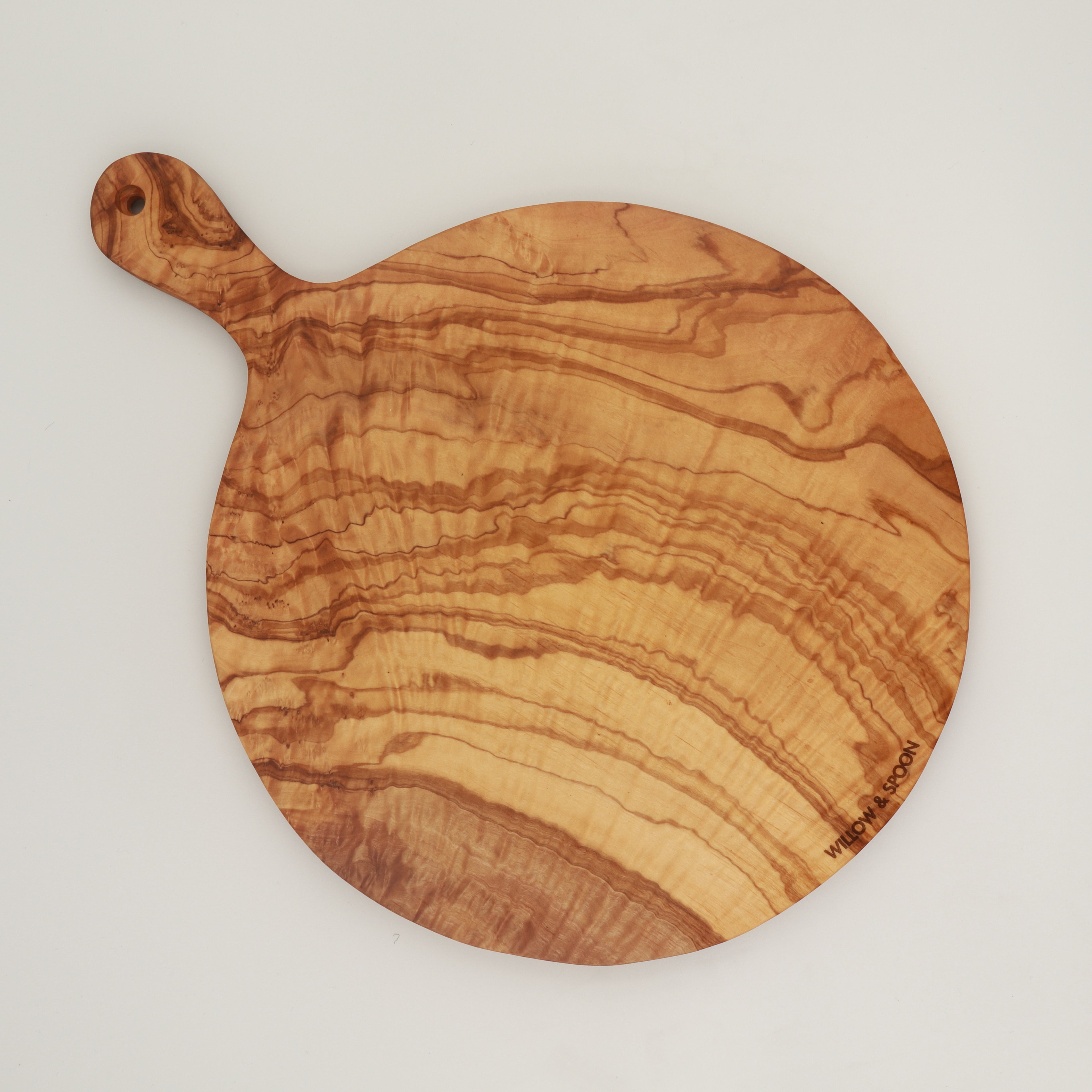 Overhead view of handcrafted Tunisian olive wood round cutting board with handle, featuring the Willow & Spoon engraved mark on a white background.