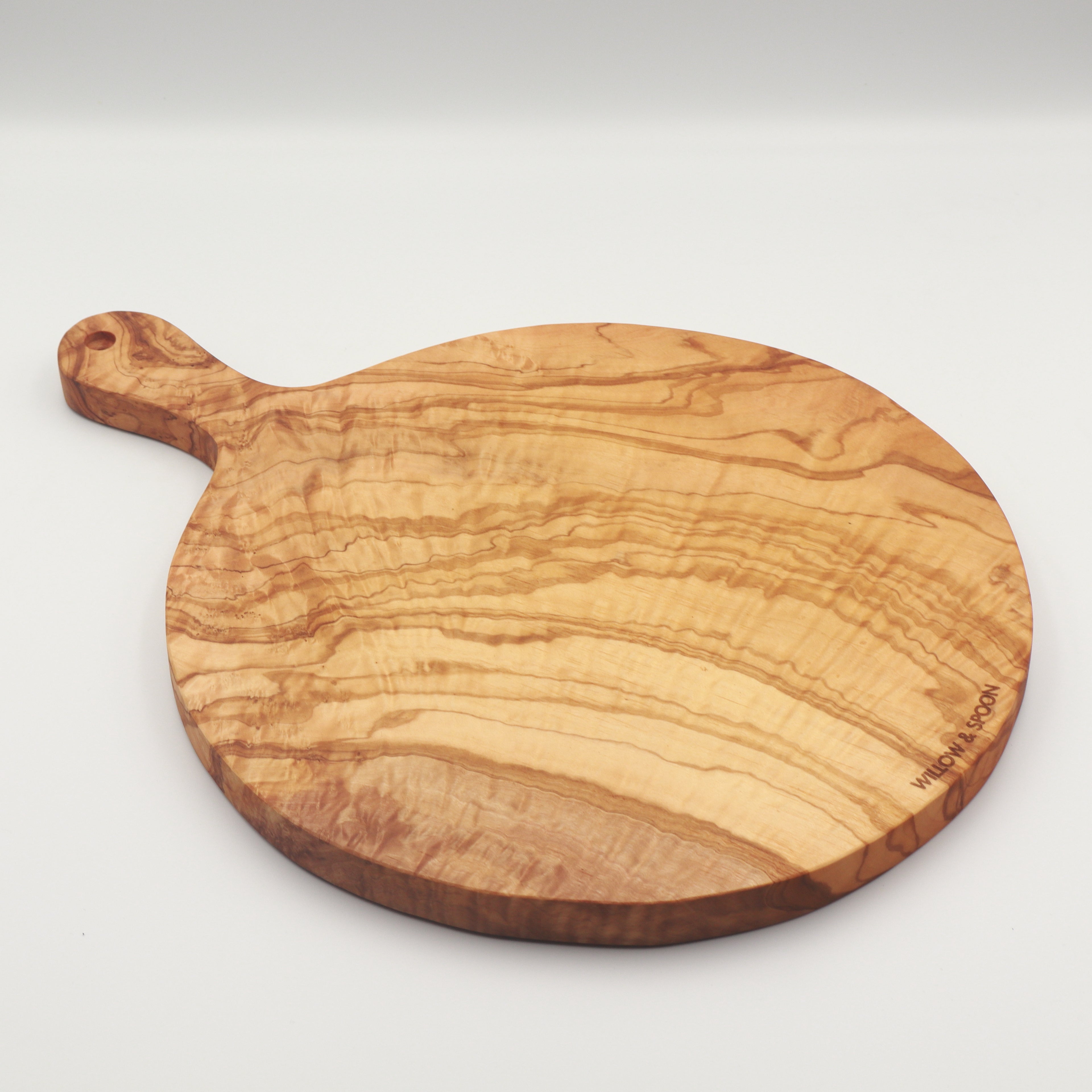Handcrafted Tunisian olive wood round cutting board with handle on a white background, featuring the Willow & Spoon engraved mark.