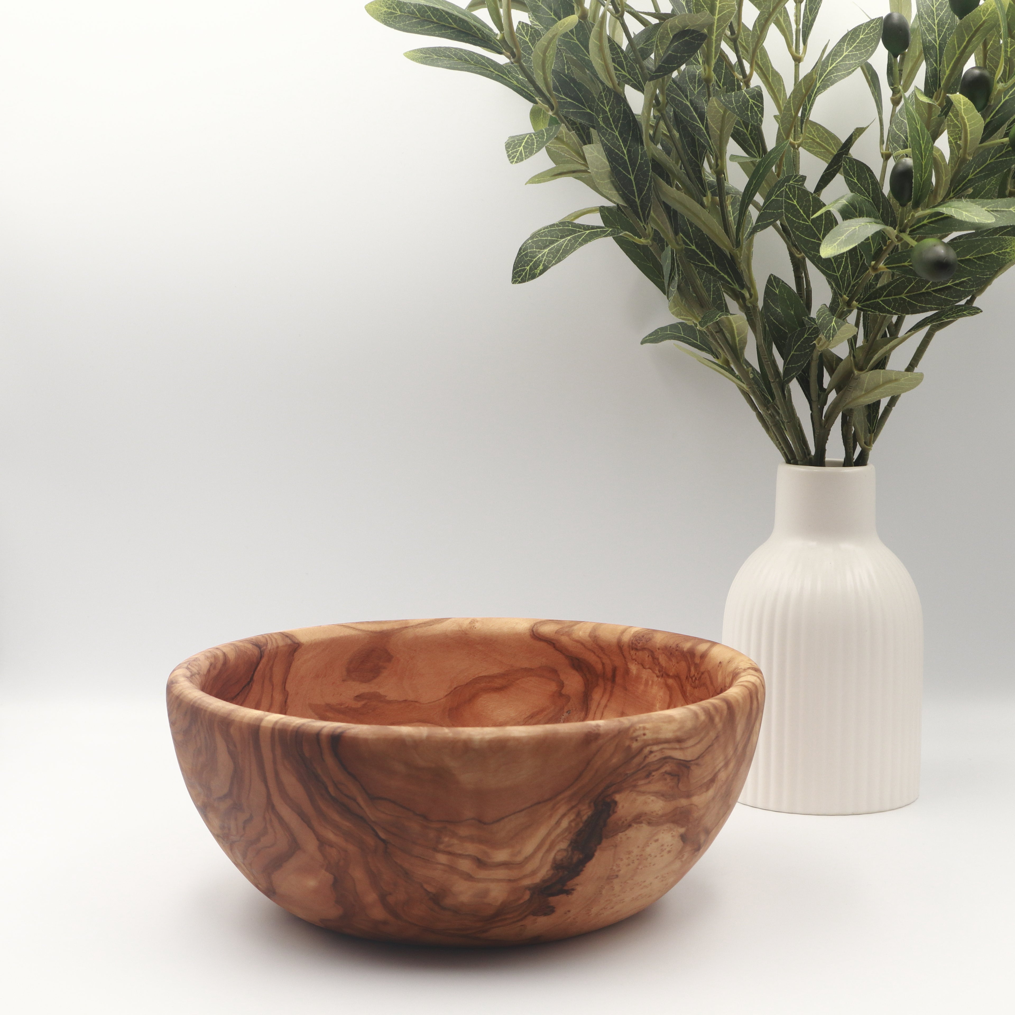 Handcrafted Tunisian olive wood salad bowl, styled on a white counter beside a vase of olive branches.
