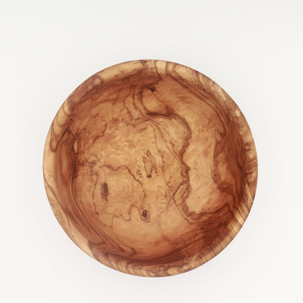 Overhead view of a handcrafted Tunisian olive wood salad bowl showing the interior grain on a white background.