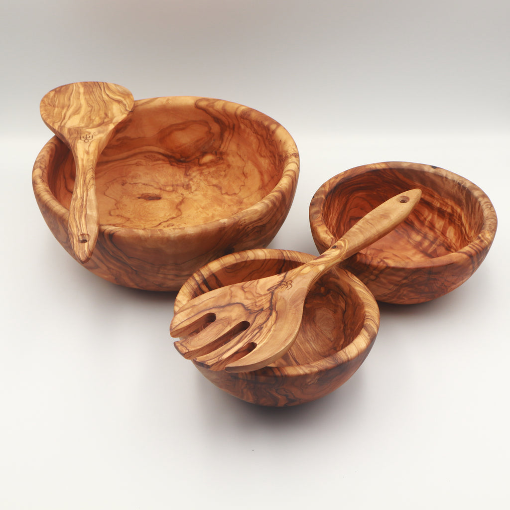 Angled view of handcrafted Tunisian olive wood salad set with large serving bowl, two side bowls, and salad servers resting inside.