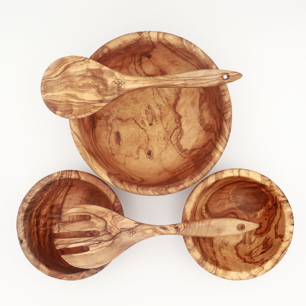 Overhead view of handcrafted Tunisian olive wood salad set with serving bowl, two side bowls, and salad servers resting inside.