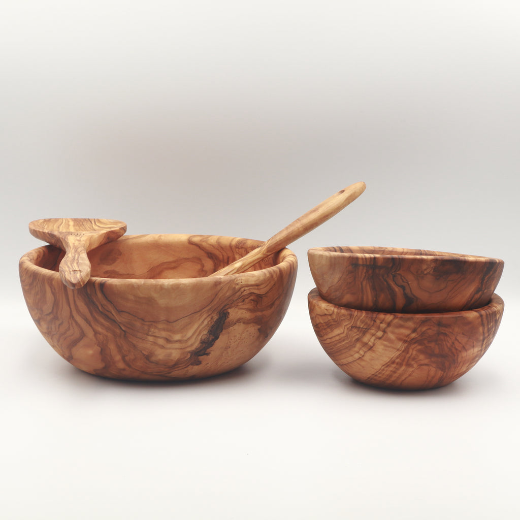 Angled view of a handcrafted Tunisian olive wood salad set with large serving bowl, salad servers, and two stacked side bowls on a white background.