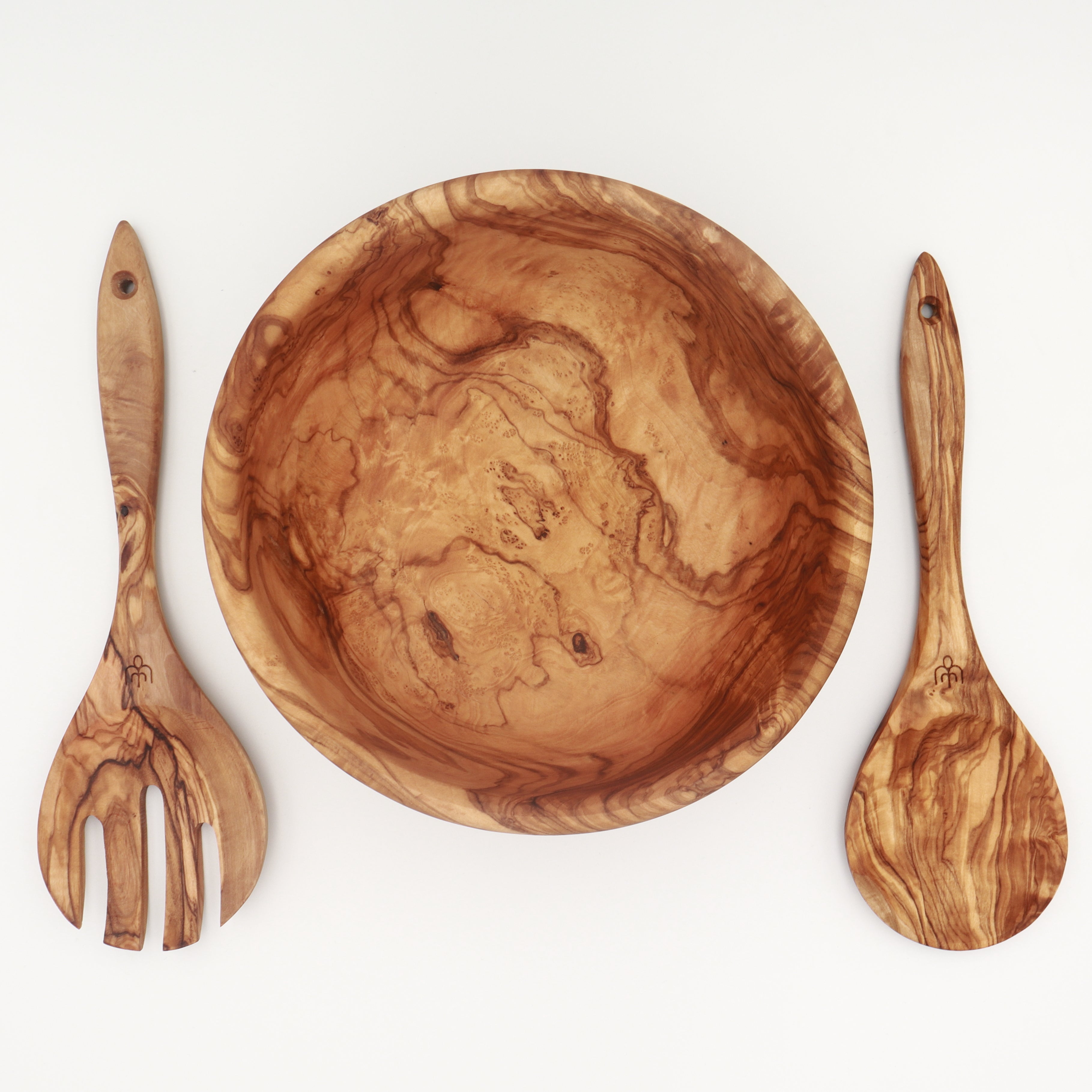 Overhead view of a handcrafted Tunisian olive wood salad bowl with a server fork and spoon arranged on either side on a white background.