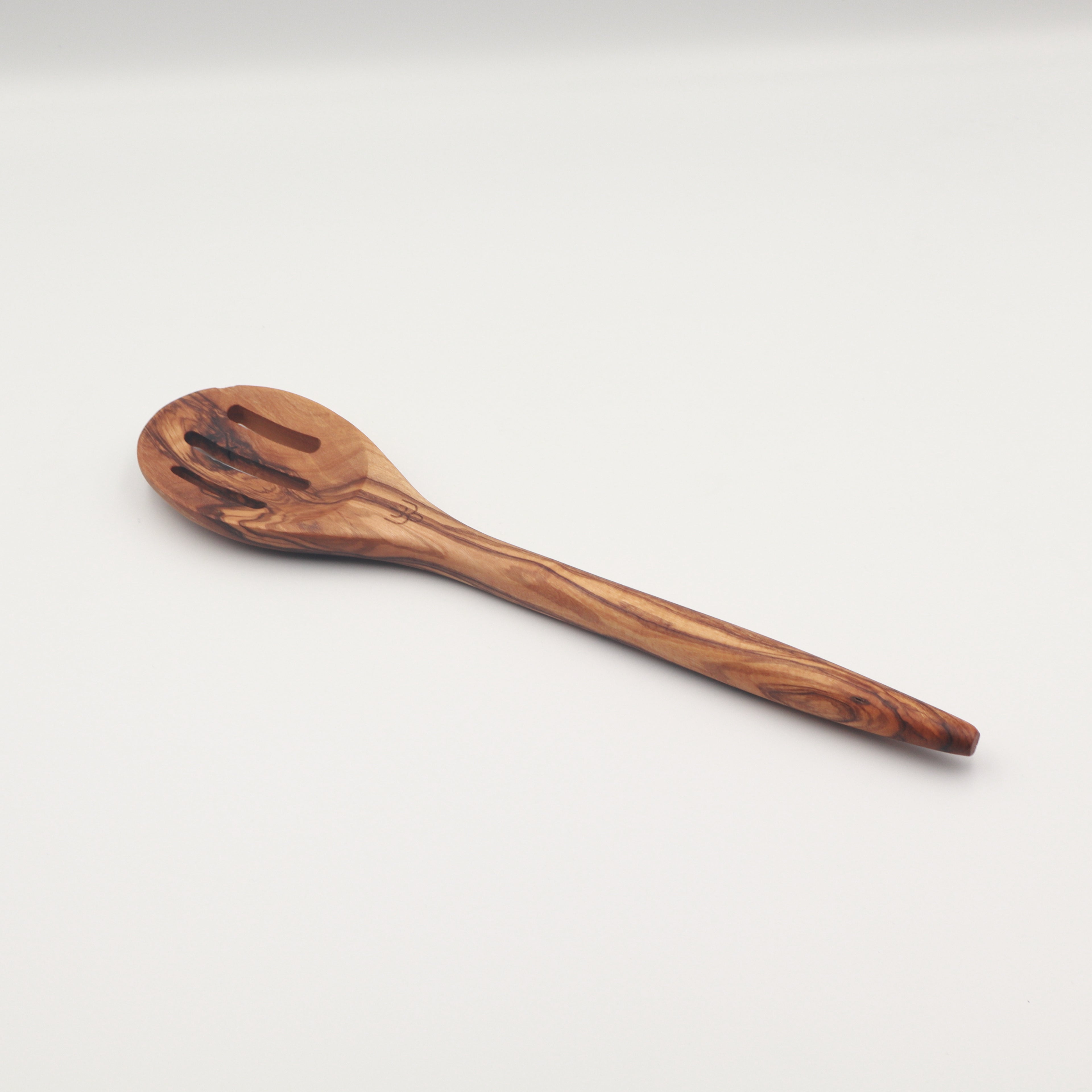 Handcrafted Tunisian olive wood slotted spoon shown on a white background highlighting the natural grain.