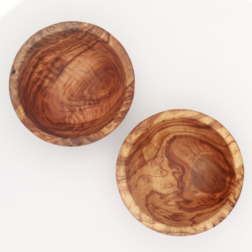 Overhead view of two handcrafted Tunisian olive wood small bowls showing the interior grain on a white background.