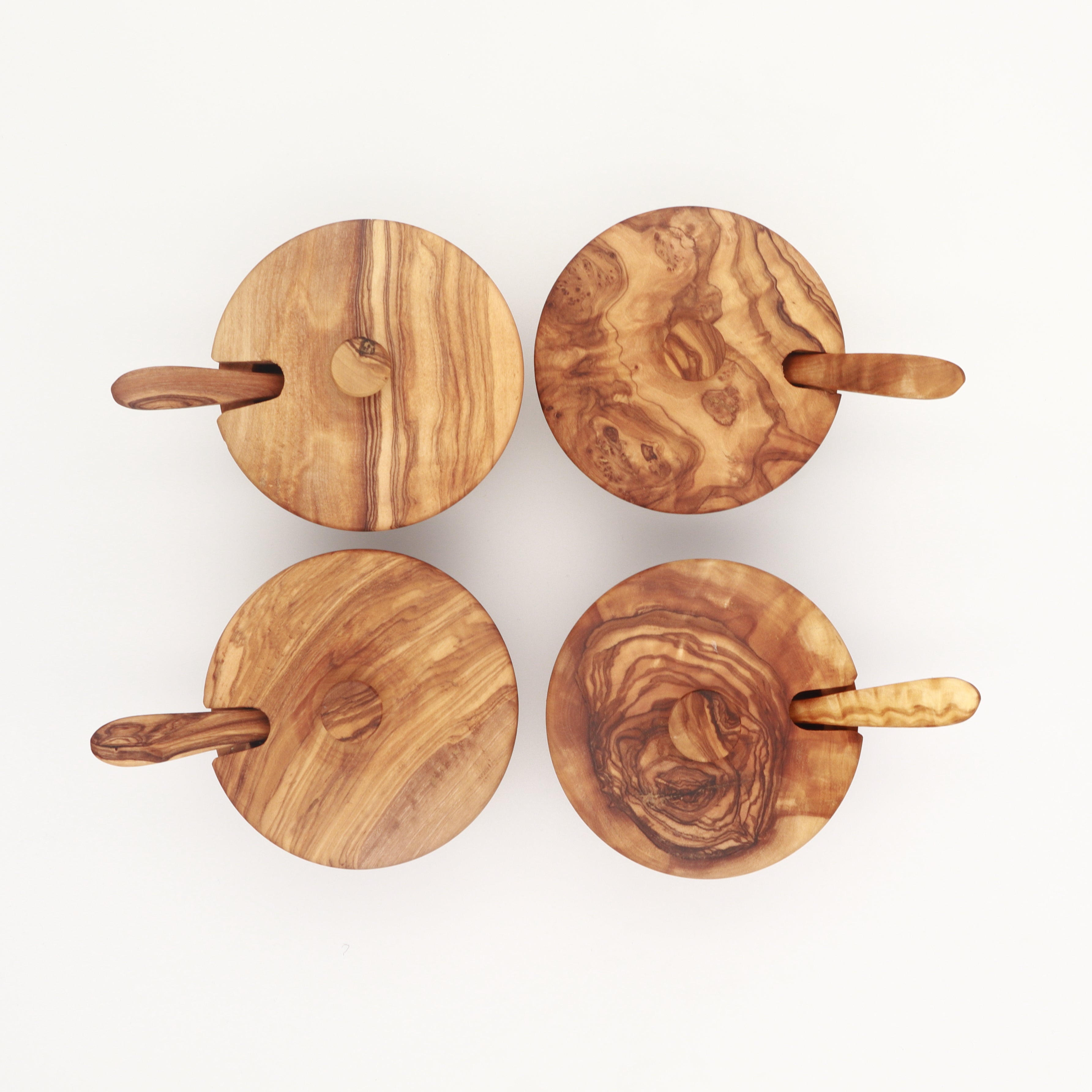 Four handcrafted olive wood spice boxes with swivel lids and small spoons, showing varied grain patterns.