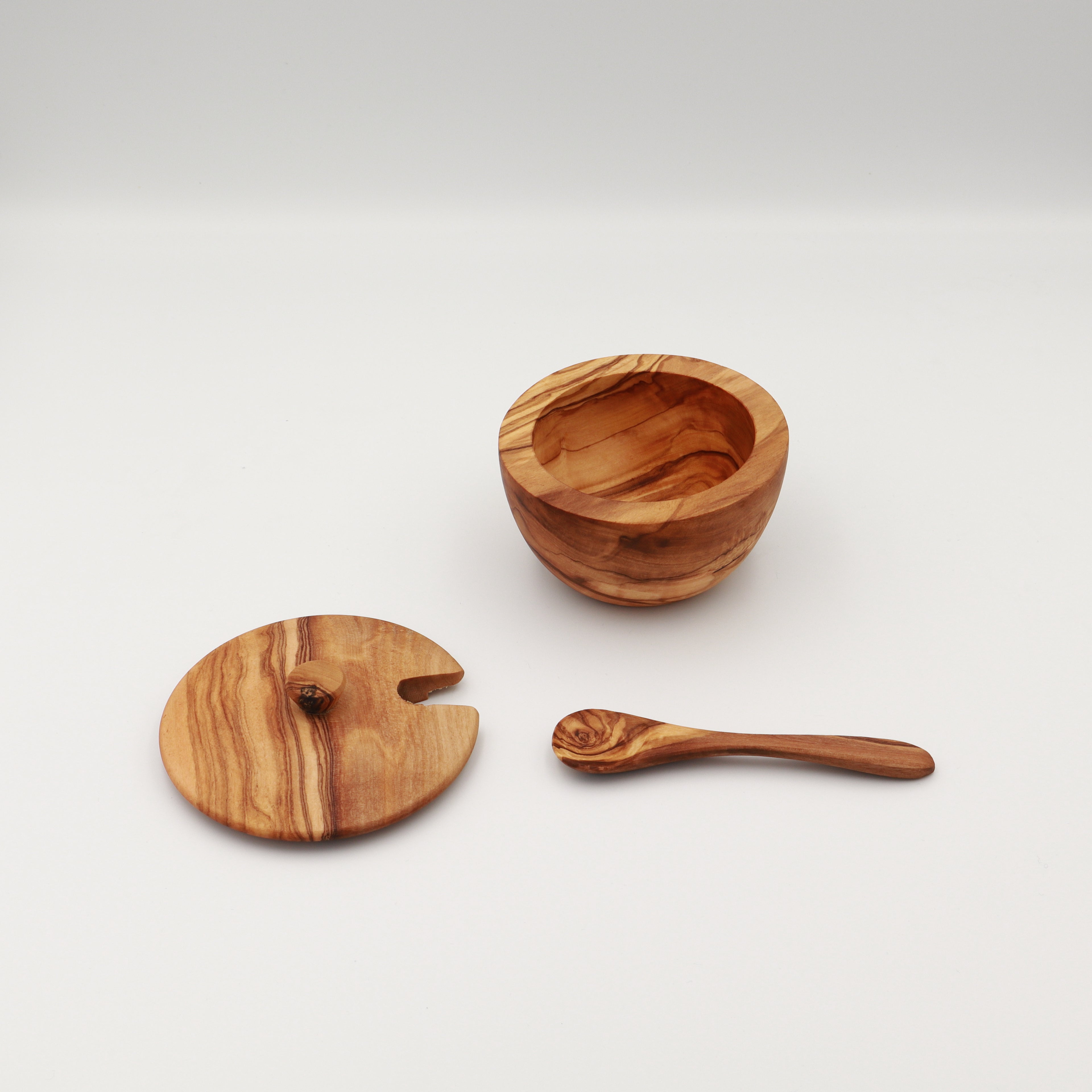 Angled view of a handcrafted Tunisian olive wood spice box shown disassembled with the open box, lid, and serving spoon on a white background.