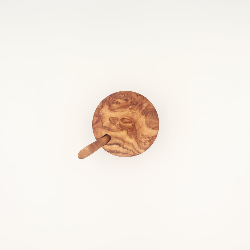 Overhead view of a handcrafted Tunisian olive wood spice box with lid and serving spoon on a white background.
