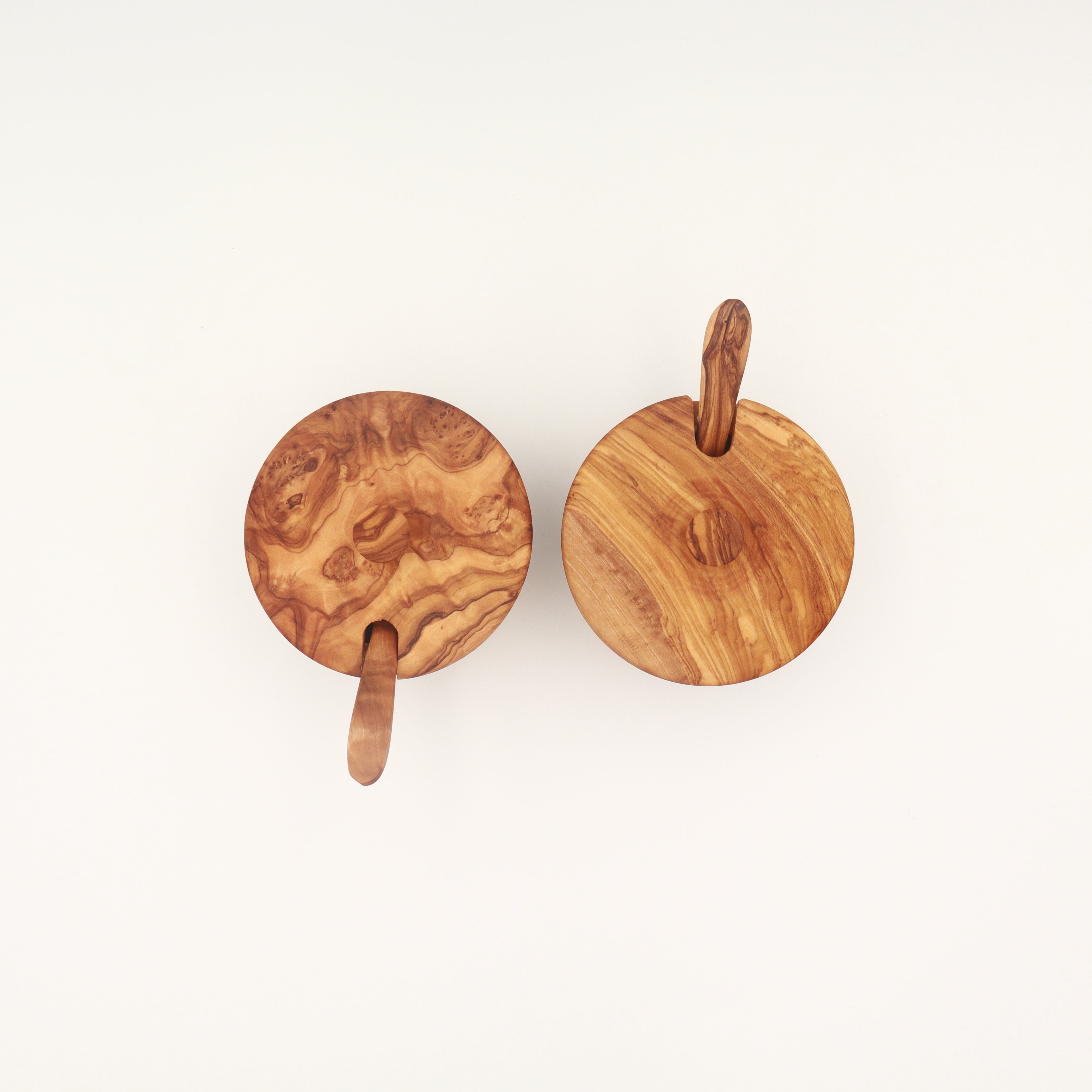 Overhead view of a pair of handcrafted Tunisian olive wood spice boxes with lids and serving spoons on a white background.