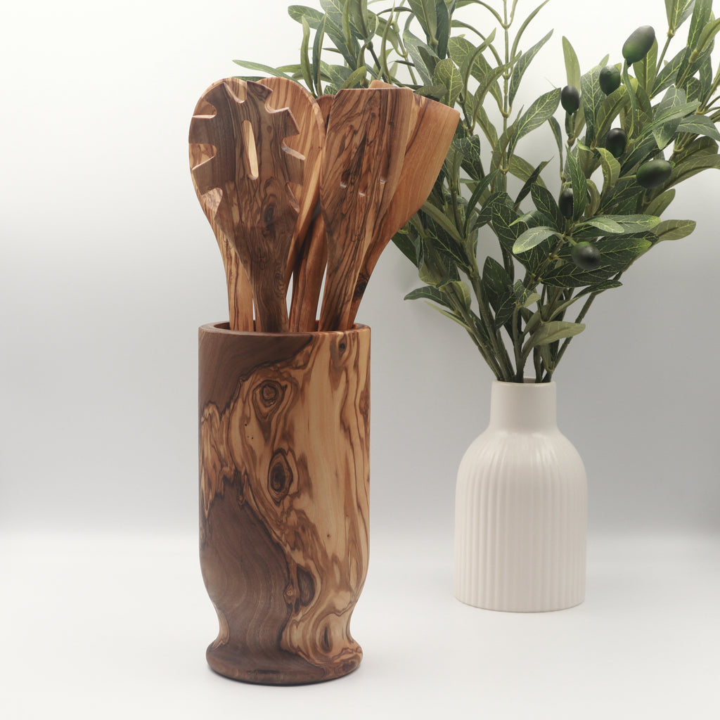  Handcrafted Tunisian olive wood utensil holder filled with six cooking utensils, styled on a white counter beside a vase of olive branches.