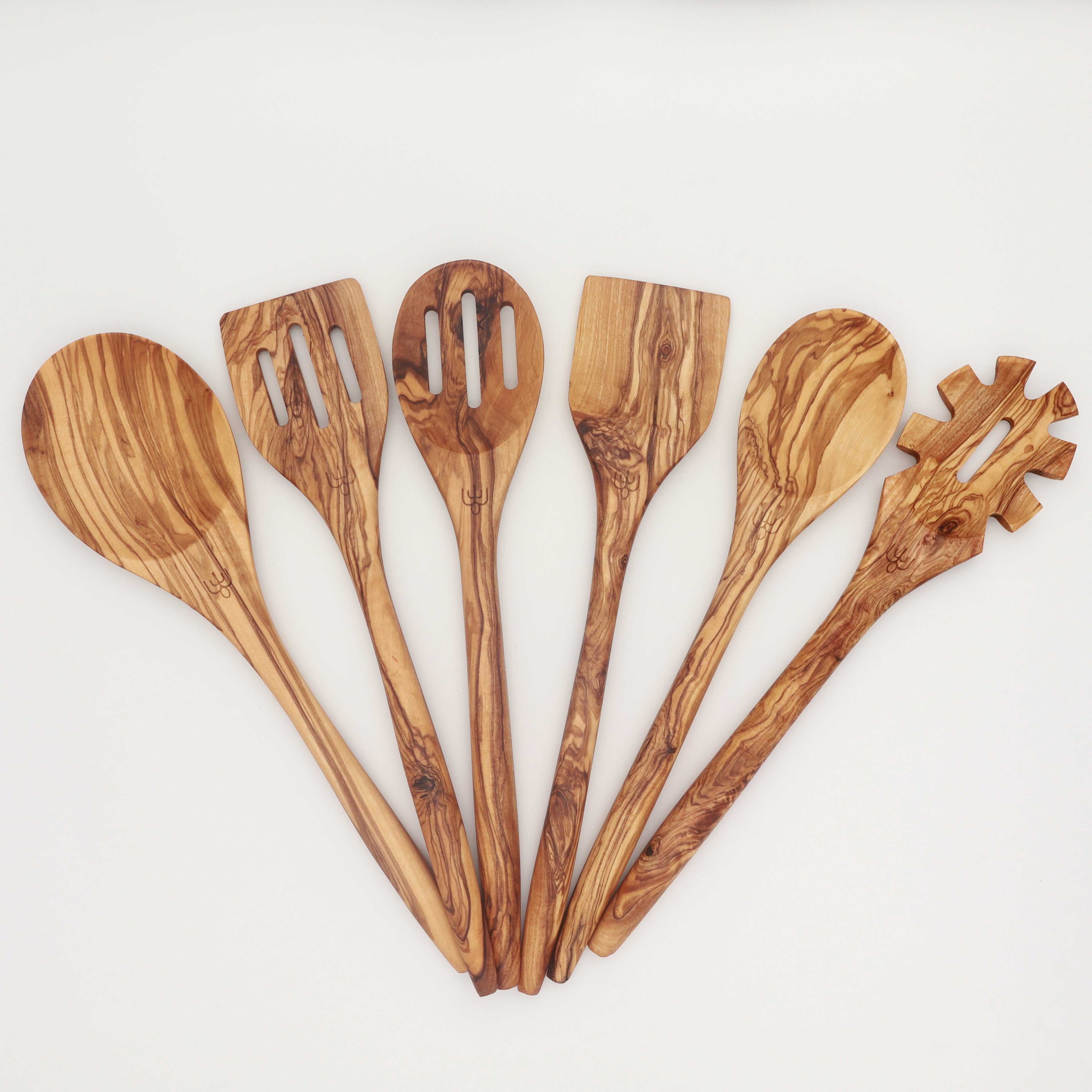Handcrafted Tunisian olive wood six-piece utensil set with cooking spoons, slotted spoons, spatula, and pasta server arranged in a fan on a white background.