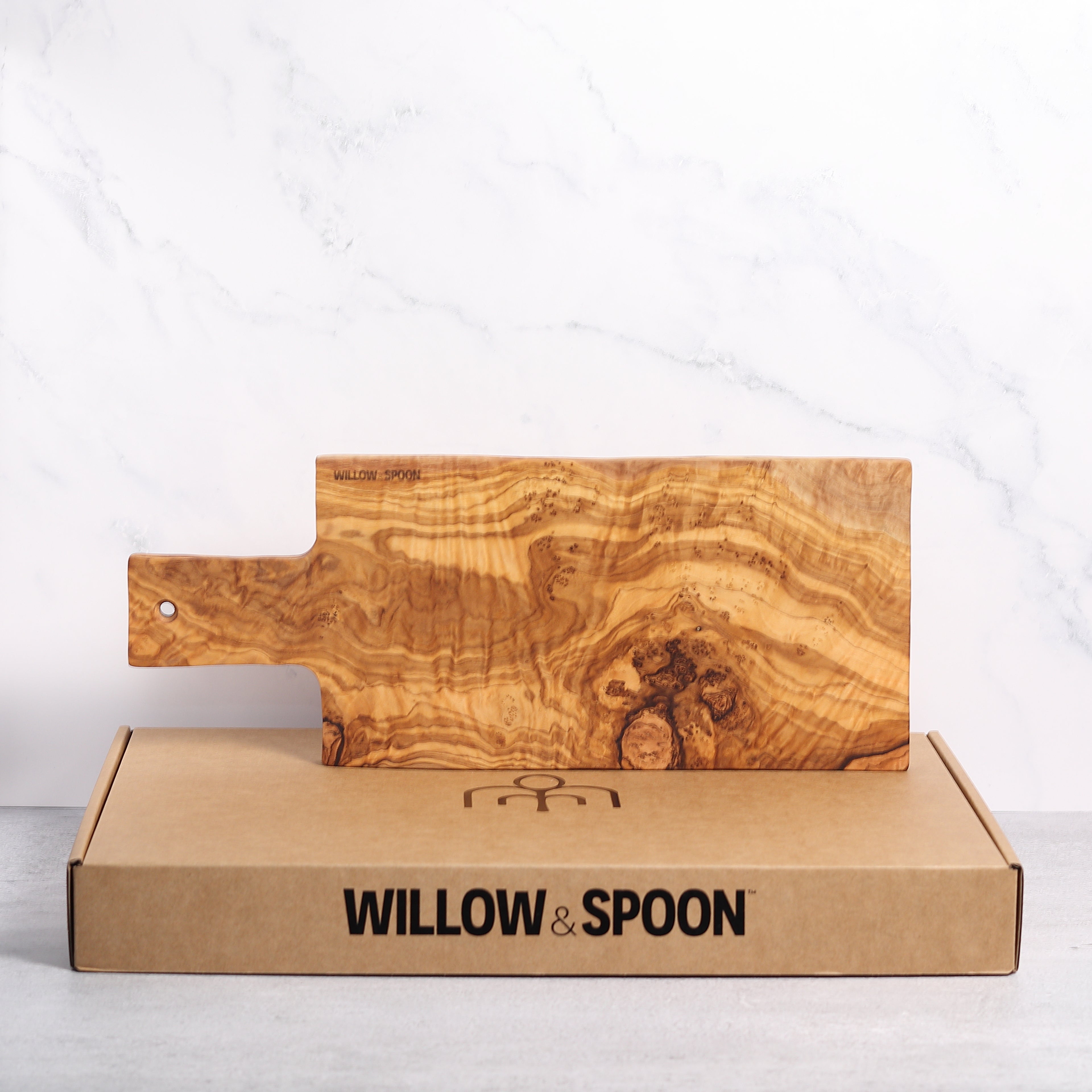 Rectangular olive wood serving board with handle displayed on a Willow & Spoon branded box against a marble background