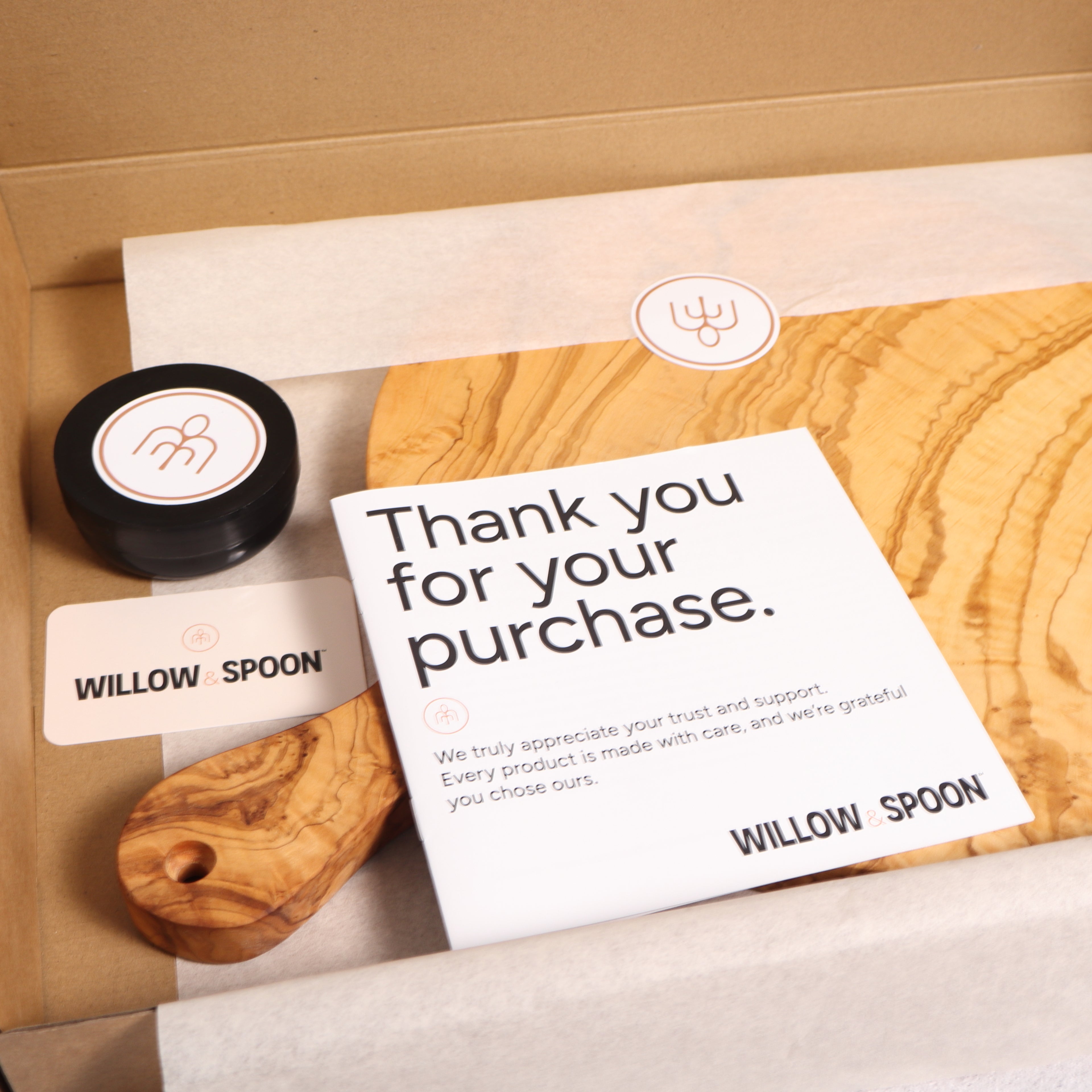 Round olive wood serving board with handle packaged in a Willow & Spoon gift box with tissue paper, branded coaster, and thank you card