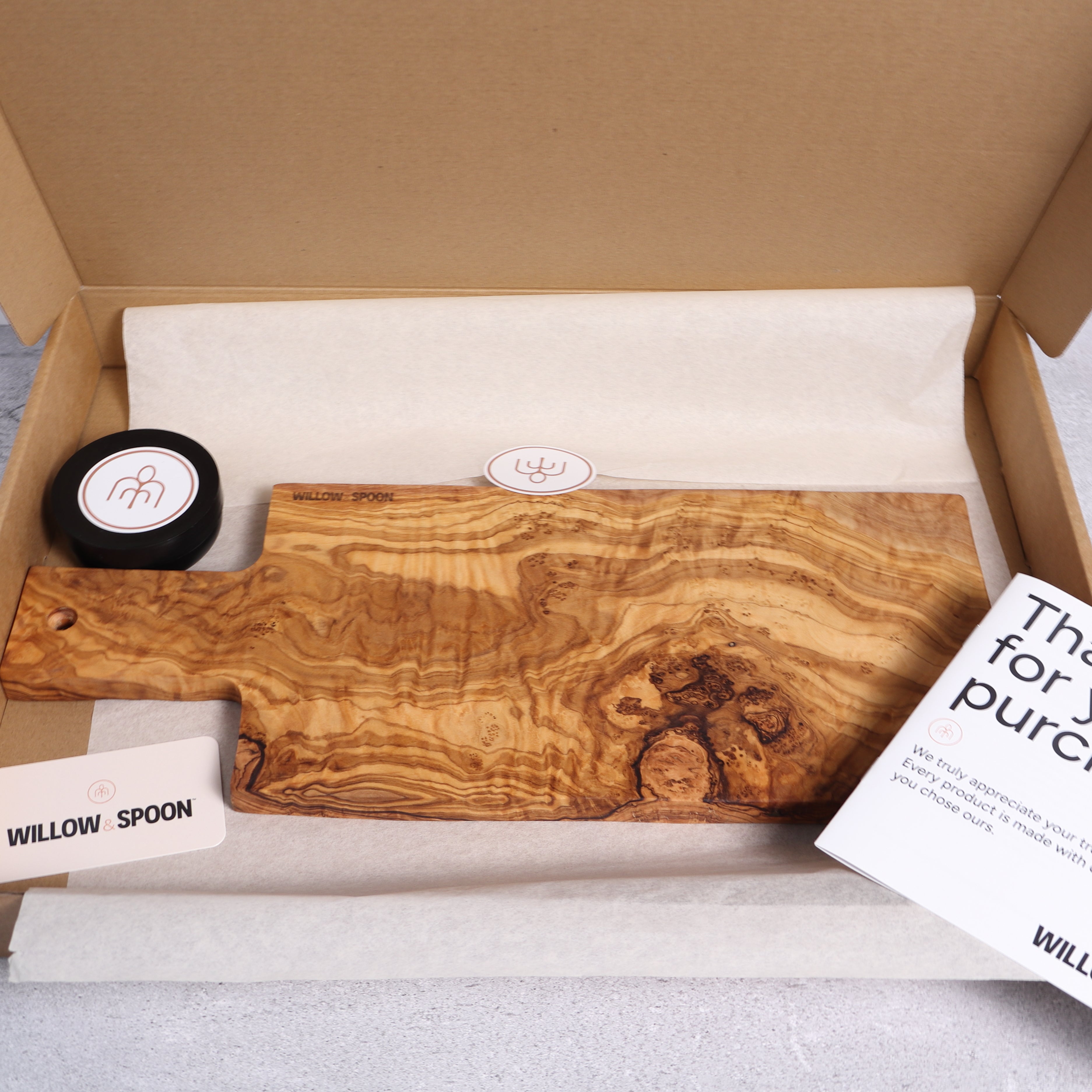 Rectangular olive wood serving board with handle packaged in a Willow & Spoon gift box with tissue paper, branded coaster, and thank you card