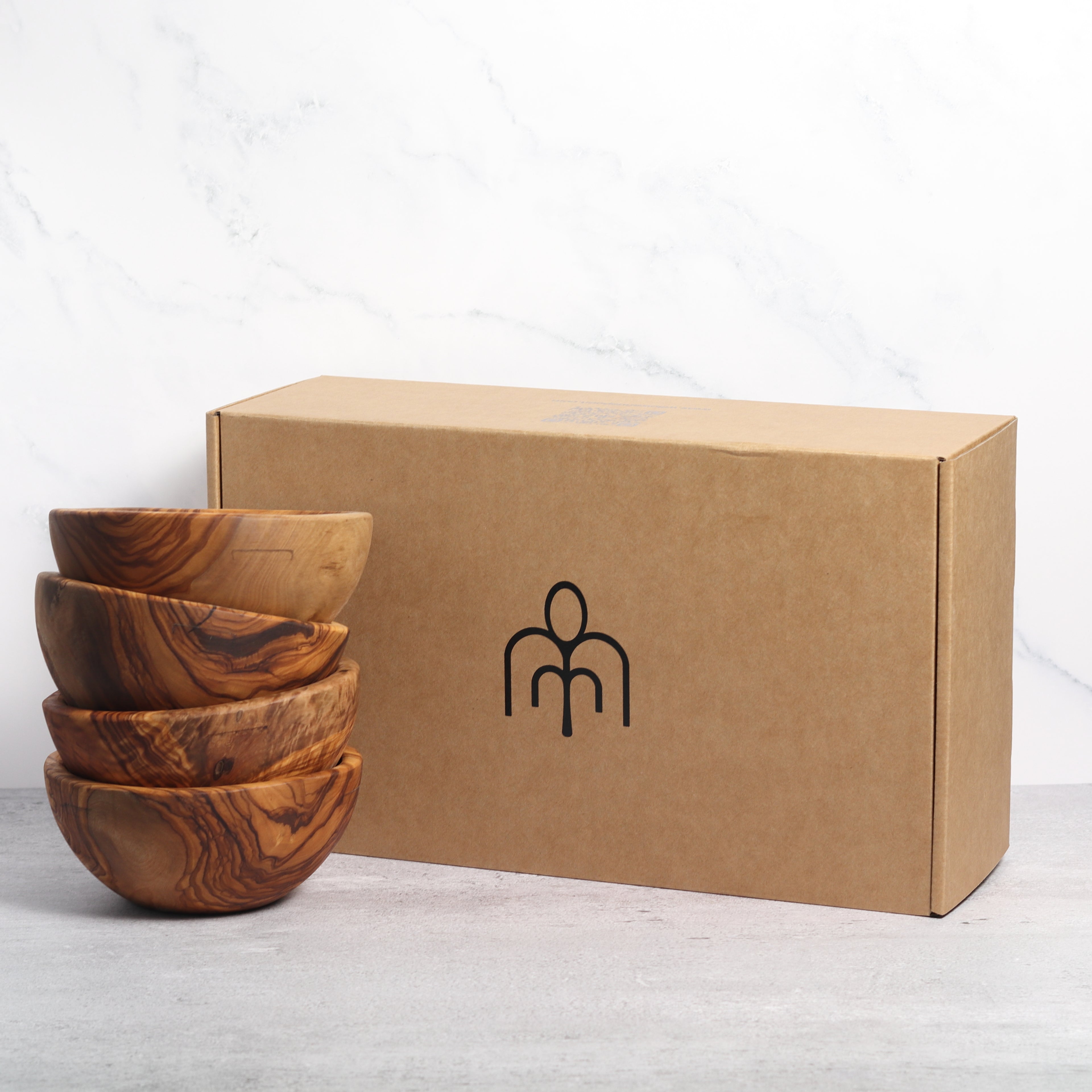 Four stacked olive wood bowls next to a Willow & Spoon branded box against a marble background