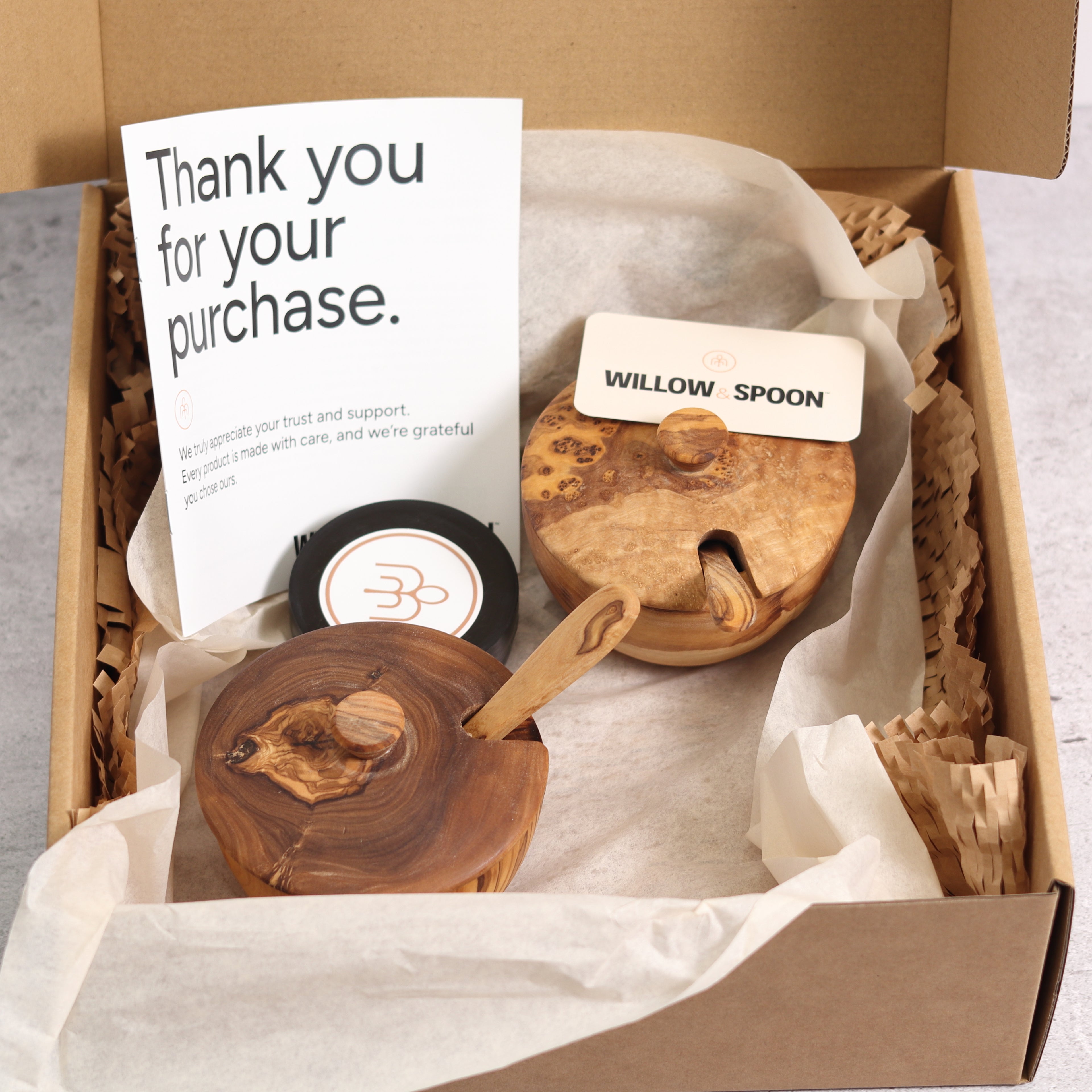 Two olive wood spice boxes with lids and spoons packaged in a Willow & Spoon gift box with tissue paper, branded coaster, and thank you card